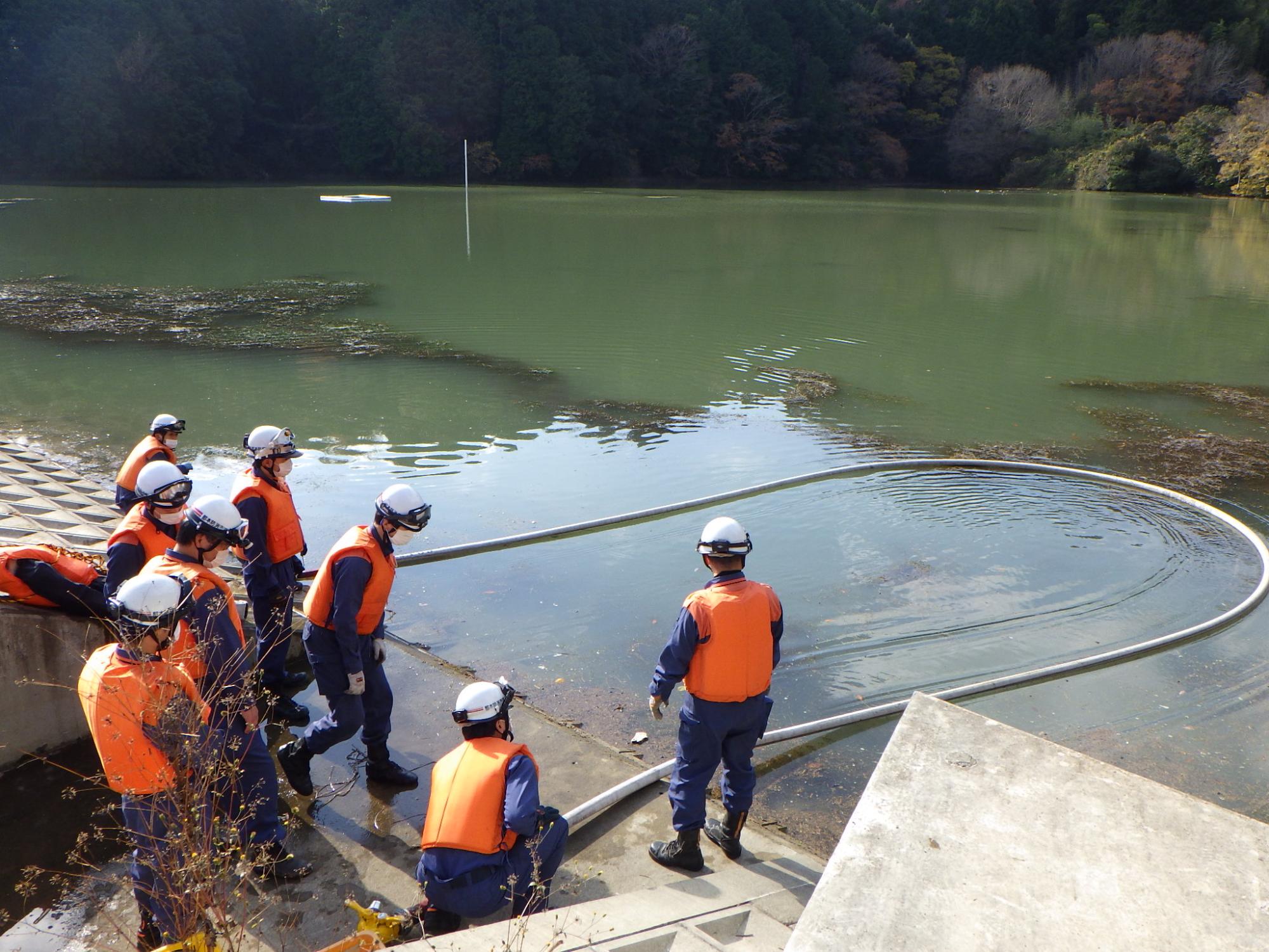消防用ホースに空気を入れ、大きな浮環を作成し、池へ浮かべている画像